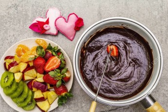 Chocolate fondue. Assorted fresh fruits, two types of chocolate, felt hearts. Ingredients for cooking a sweet romantic dessert. Stone concrete background
