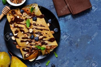 Homemade thin pancakes with caramelized pears, chocolate sauce and nuts on a concrete background.
