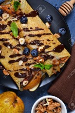 Homemade thin pancakes with caramelized pears, chocolate sauce and nuts on a concrete background.
