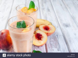 refreshing-summer-smoothie-or-milkshake-with-apricot-peach-and-banana-mint-yogurt-in-glass-with-ingredients-on-white-wooden-table-copy-space-top-M9P42N.jpg
